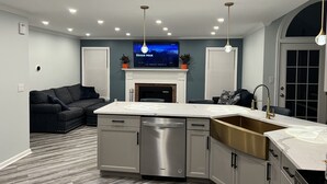 A modern kitchen with a built-in island, stainless steel appliances, and a large flat-screen TV above the fireplace. - 4 min drive to the beach (Lewes)