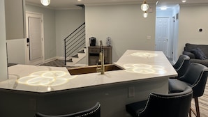 A modern kitchen with a central island, pendant lighting, and a staircase leading to another level. - 4 min drive to the beach (Lewes)