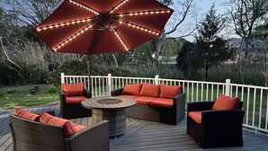 An outdoor deck with a round table, wicker furniture, and a large umbrella. - 4 min drive to the beach (Lewes)
