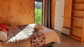 A wooden room with a bed, a radiator, and a view of a green landscape.