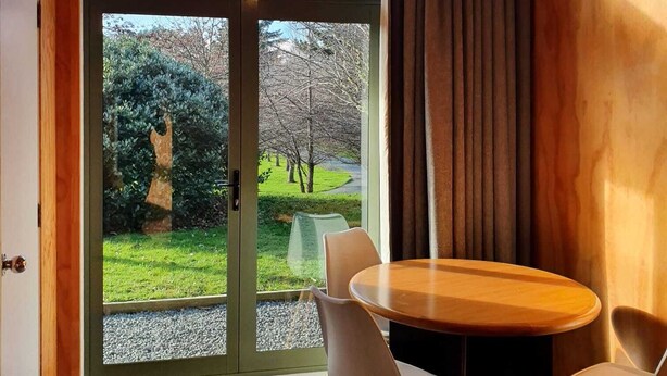 A dining area with a wooden table and chairs, a hanging light fixture, and a view of a garden through a glass door.