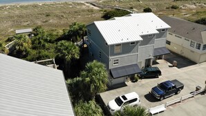 Un edificio de dos pisos con techo metálico, rodeado de un estacionamiento y vistas a la playa.