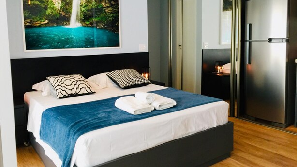 Une chambre moderne avec un lit, un grand tableau encadré représentant une cascade, une armoire noire et un réfrigérateur en acier inoxydable.