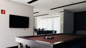 Une table de billard avec des billes, un téléviseur fixé au mur et un panneau indiquant l’emplacement d’un extincteur.