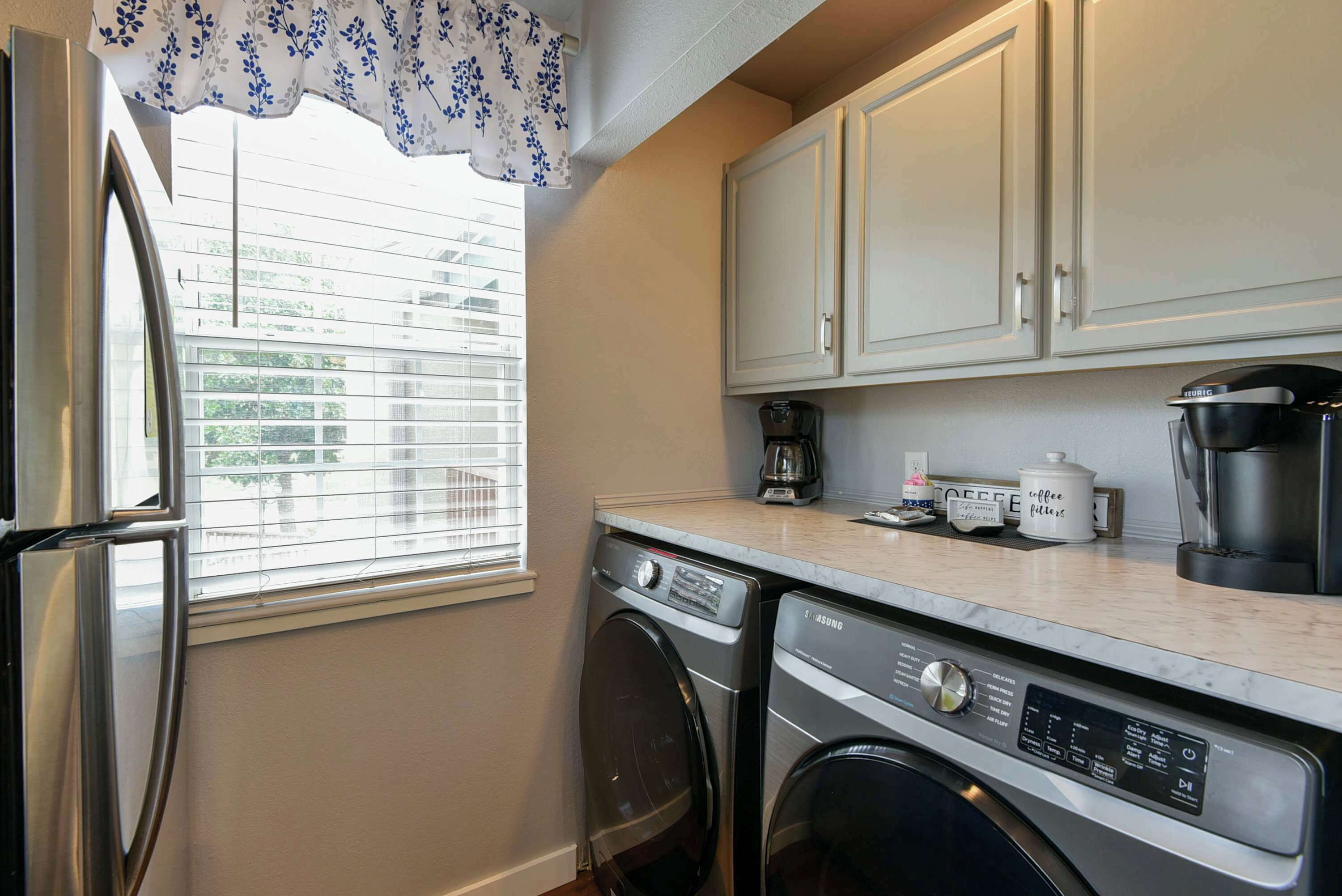 A compact kitchen with a washing machine, a coffee maker, and a refrigerator.