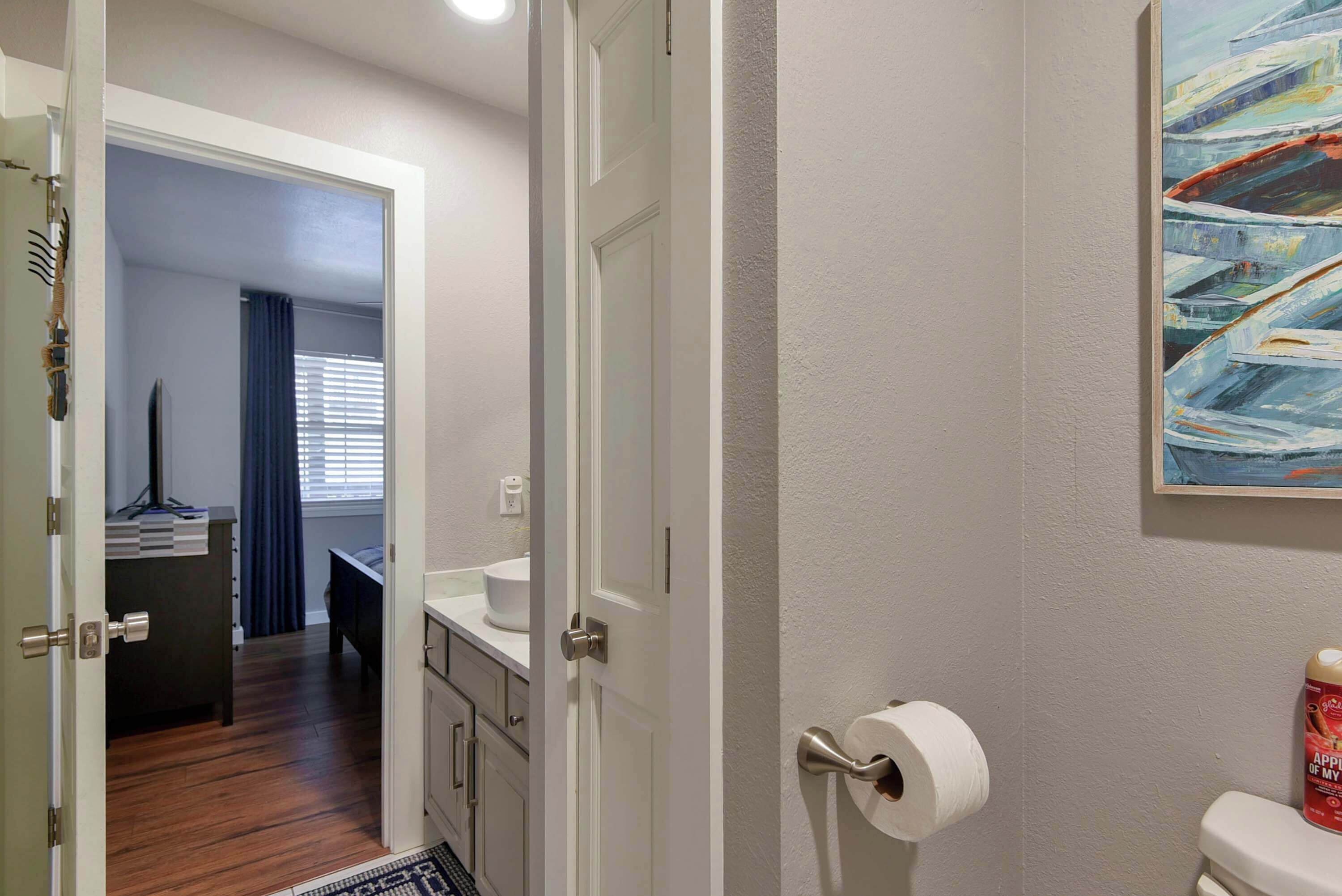 A bathroom with a toilet, a roll of toilet paper, and a painting on the wall.