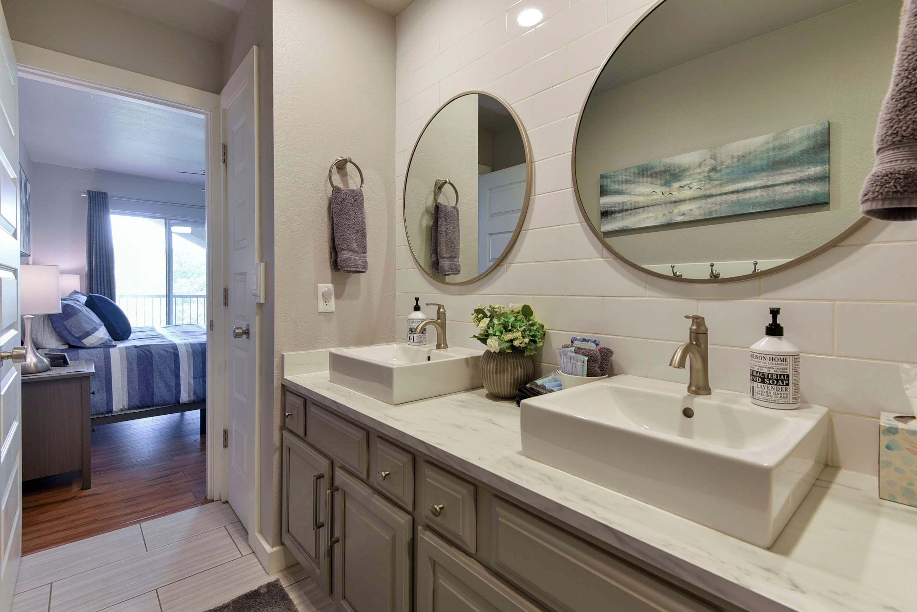A modern bathroom with two sinks, a large mirror, and a painting on the wall.