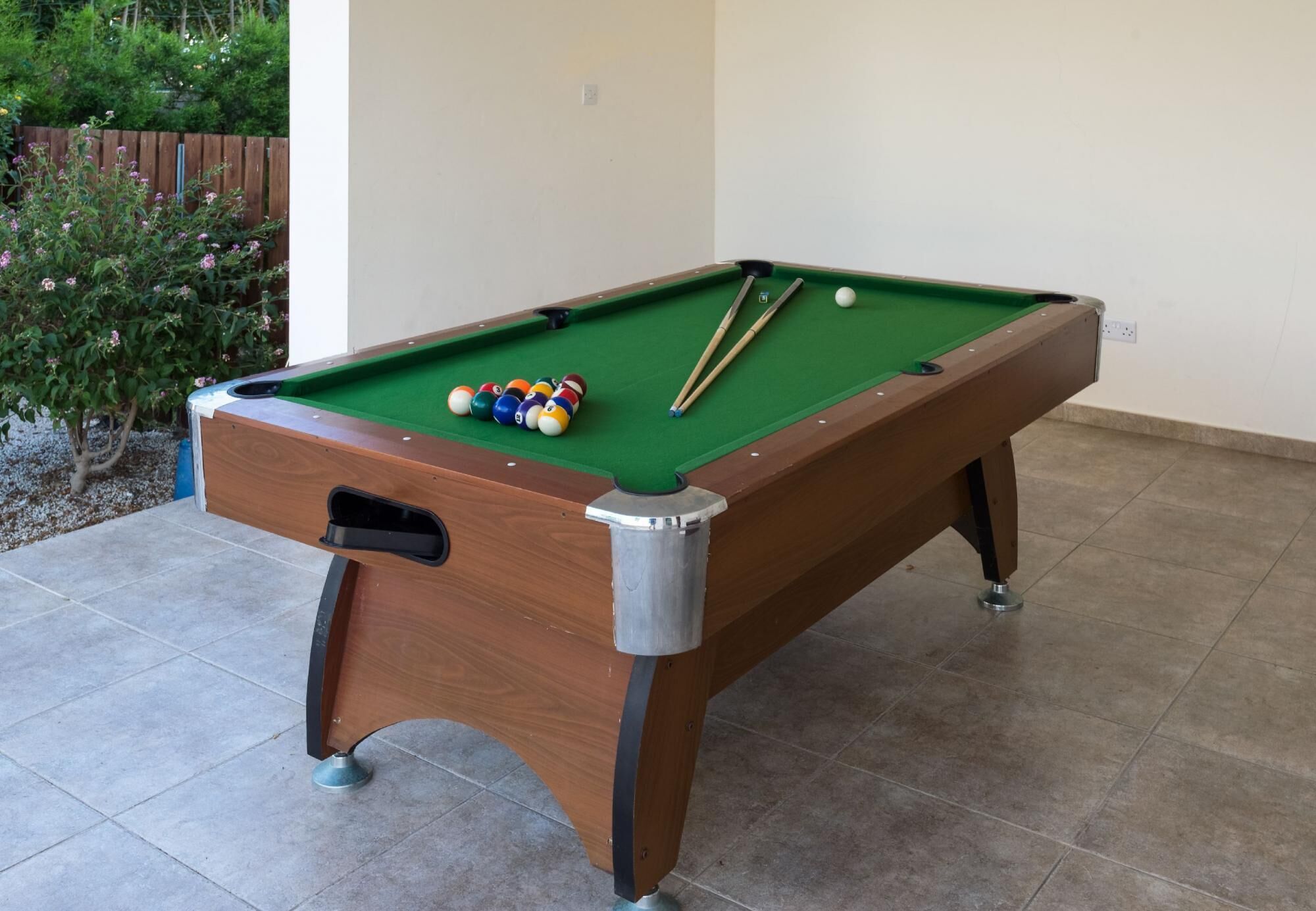 Ein Billardtisch mit Kugeln und Spielstöcken, ein Holzschrank und ein gefliester Boden.