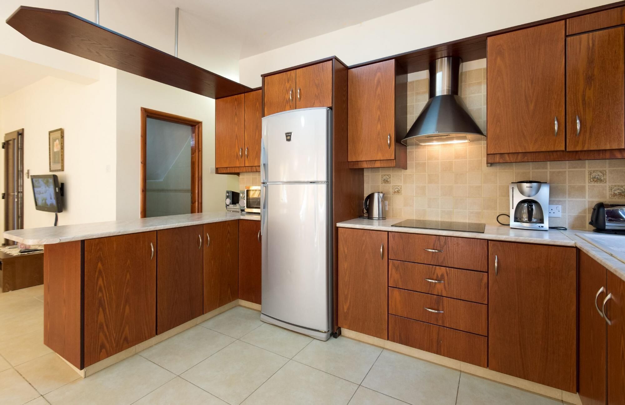 A modern kitchen with wooden cabinets, a stainless steel refrigerator, a coffee maker, and a microwave.