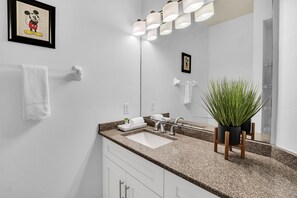 A modern bathroom with a granite countertop, a white sink, a mirror, and a Mickey Mouse framed picture.