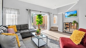 Un salon moderne avec un canapé gris, un fauteuil rouge, une table basse en verre et un téléviseur fixé au mur.