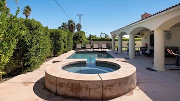 A pool area with a circular hot tub, lounge chairs, and a covered patio.