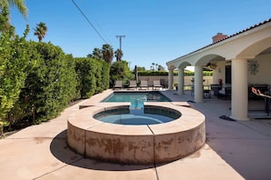 A pool area with a circular hot tub, lounge chairs, and a covered patio.