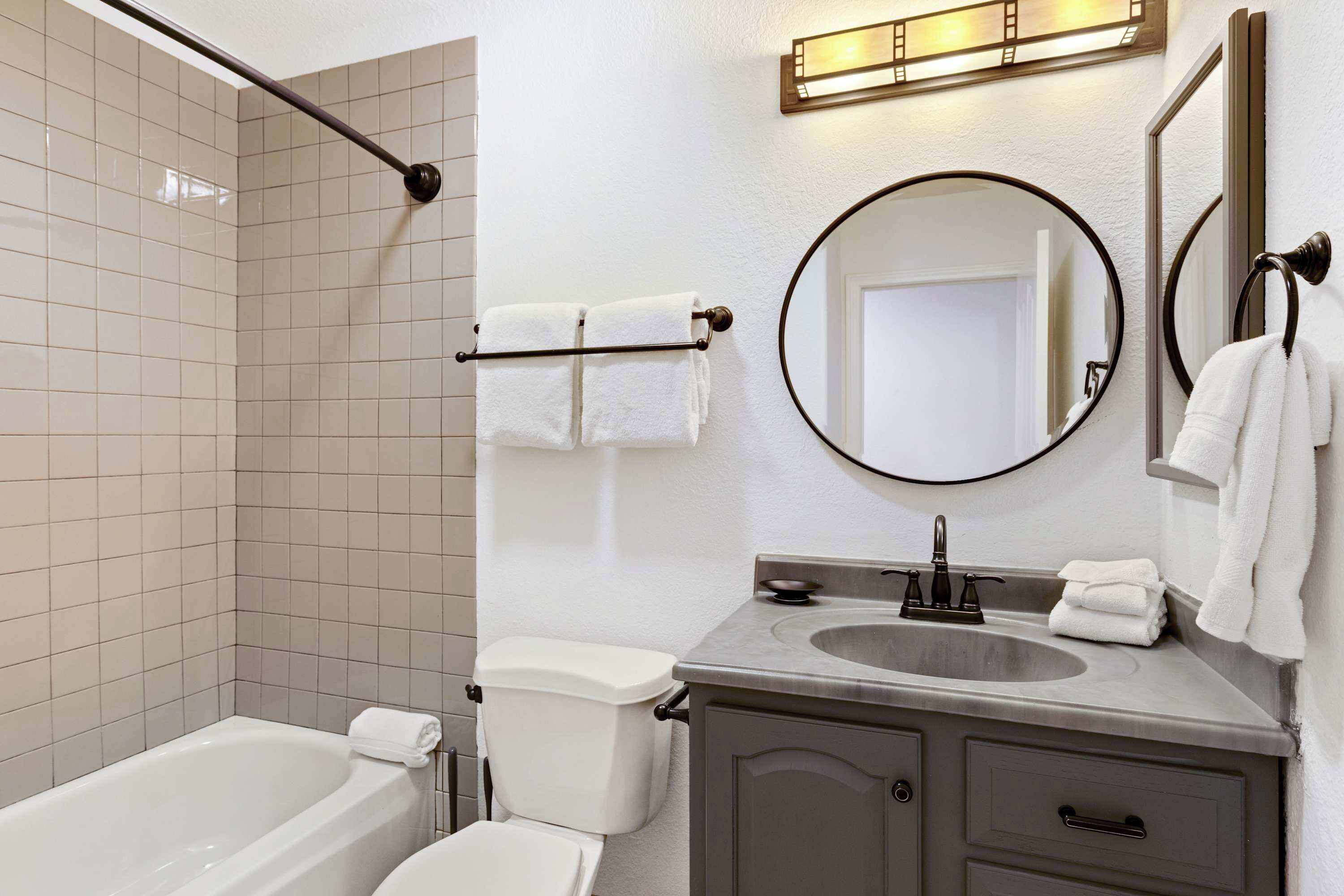 A modern bathroom with a bathtub, toilet, sink, and two mirrors.