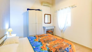 Une chambre à coucher comprenant un lit, une armoire, un bureau, un miroir et un appareil de climatisation.