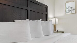 A neatly made bed with white linens and pillows, a dark headboard, and a bedside table with a lamp.