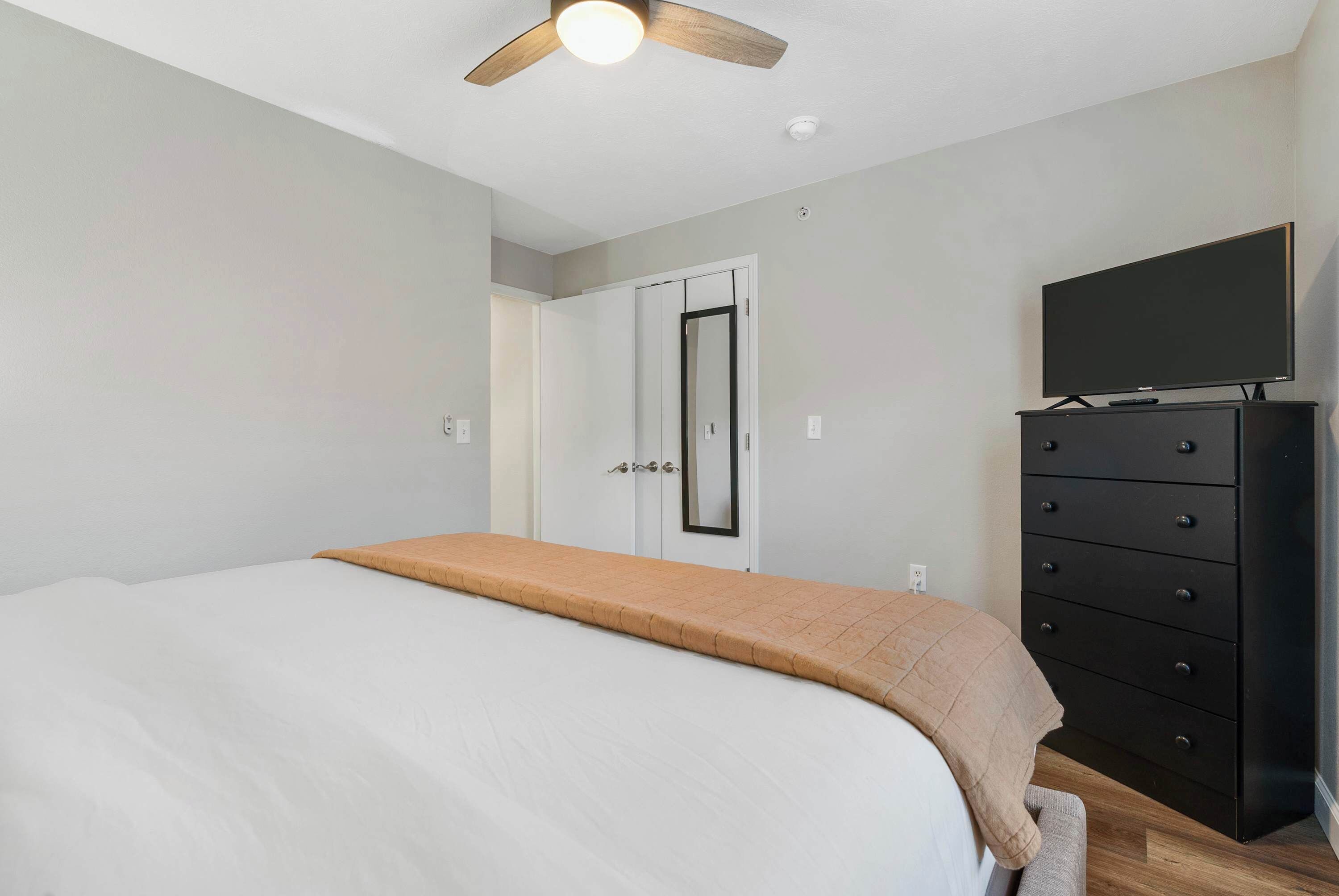 Ein Schlafzimmer mit Bett, Kommode, Fernseher und Deckenventilator.