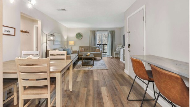 A modern living room with a dining area, wooden flooring, and a large window with curtains.