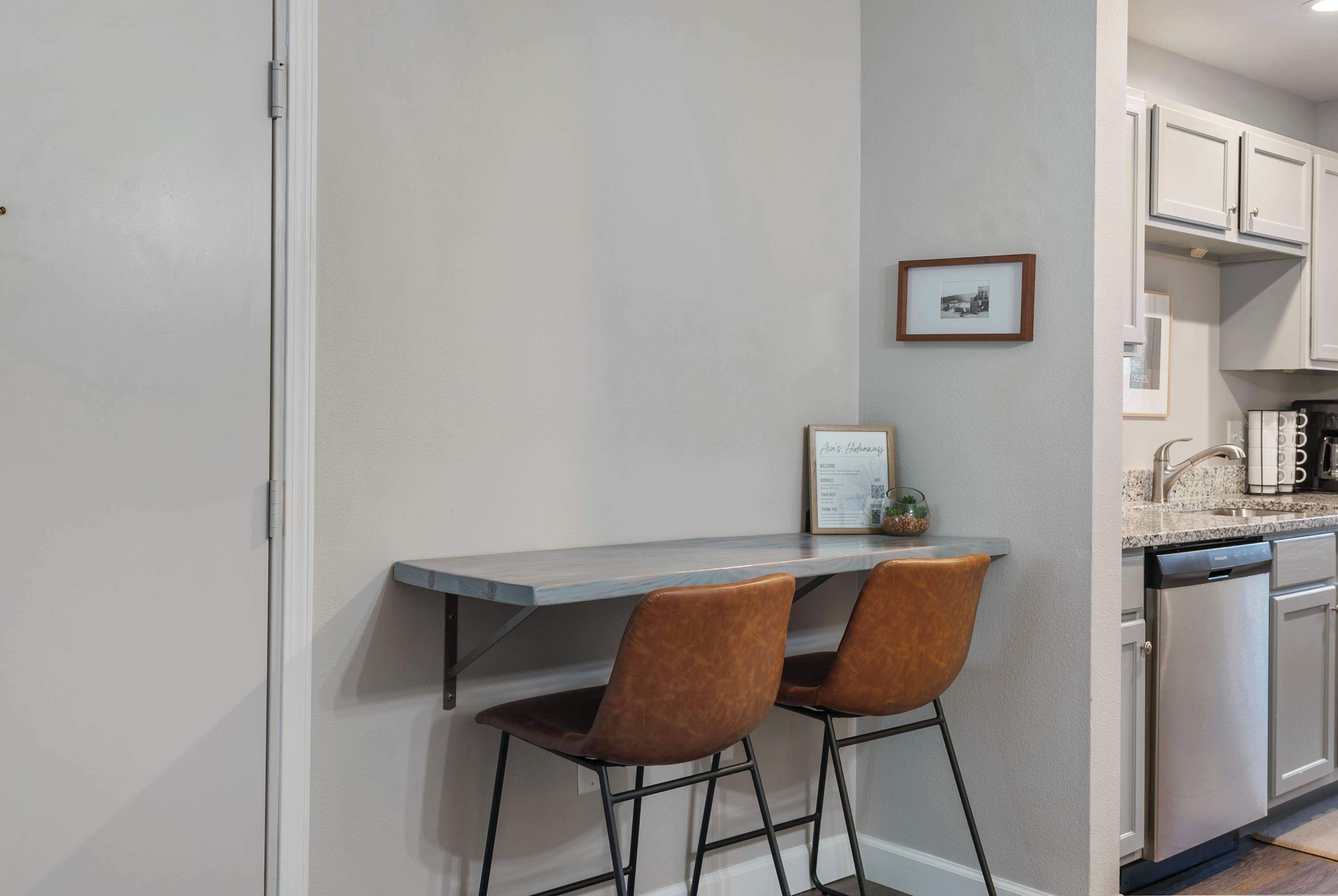 A kitchen with a grey countertop, two brown chairs, and a framed picture on the wall.