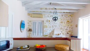 A kitchen with a stone wall, a microwave, a fruit bowl, and a woven basket. - Villa Labovitsa in Paxi (Paxos)