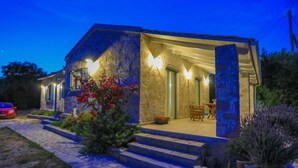 A stone house with a covered porch, steps leading to the entrance, and a car parked outside. - Villa Labovitsa in Paxi (Paxos)