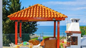 Ein überdachter Außenbereich zum Sitzen mit einem Ziegeldach, Korbmöbeln und Blick auf das Meer.