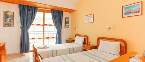 A hotel room with two beds, wooden headboards, a small desk, a chair, a window with curtains, and a painting on the wall.