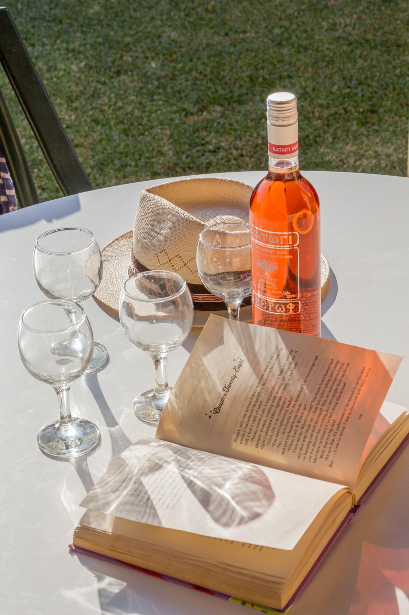 Un tavolo con una bottiglia di vino, diversi bicchieri, un libro e un cesto di vimini.