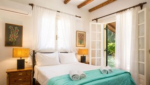 Een slaapkamer met een bed, twee nachtkastjes met lampen, een houten dressoir en een raam met gordijnen.