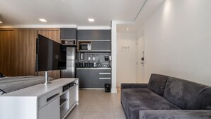 A modern, compact living space with a kitchenette, a flat-screen TV, a sofa, and a dining area. - Vi0405 Vision Augusta (São Paulo)