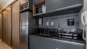A modern kitchen with dark cabinetry, a stainless steel refrigerator, a microwave, a coffee machine, and a gas stove. - Vi0405 Vision Augusta (São Paulo)