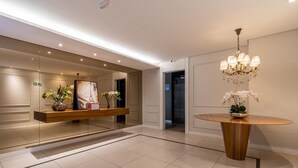 Un hall d’hôtel moderne avec un comptoir d’accueil, un lustre et une table ronde en bois sur laquelle est posée une orchidée en pot.