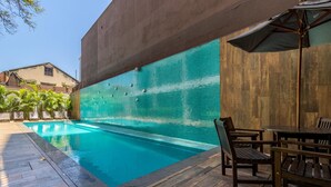 Une piscine avec un mur carrelé, une terrasse en bois et un espace salon extérieur.