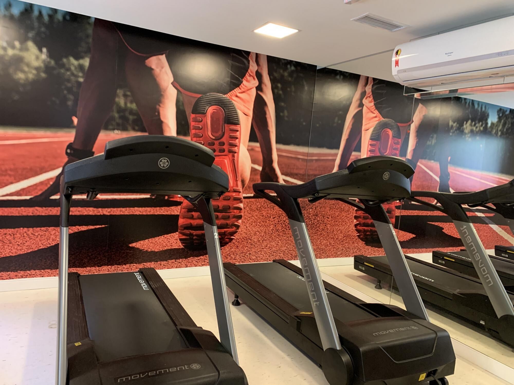 A gym with treadmills and a wall mural of athletes.