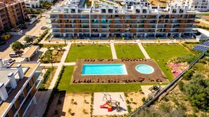 Un immeuble d’appartements moderne doté d’une piscine centrale, entouré d’une pelouse bien entretenue et d’un espace de jeux pour enfants.