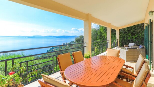 A balcony with a wooden table and chairs, overlooking a lake and greenery. - Villa Natasha in Nisaki (Corfu)