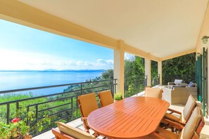 Un balcon avec une table et des chaises en bois, donnant sur un lac et une végétation luxuriante.