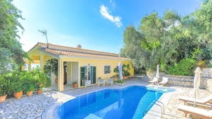 A swimming pool with stone tiles, a yellow building with a tiled roof, and potted plants. - Villa Natasha in Nisaki (Corfu)