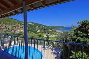 Ein Pool mit Metallgeländer, umgeben von Grün und mit Blick auf eine Küstenlandschaft mit Häusern und blauem Himmel.