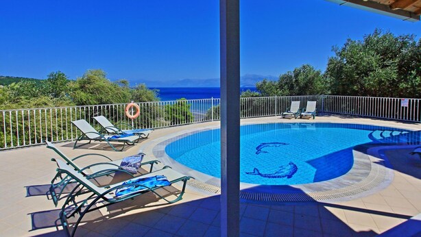 Piscina com vista para o mar, rodeada por espreguiçadeiras e um aviso de segurança.