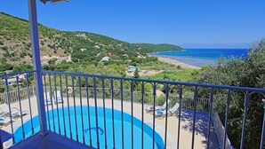 Varanda com piscina, vista para uma praia e paisagem montanhosa.