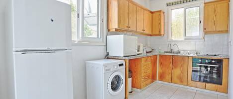 A compact kitchen with wooden cabinets, a washing machine, a microwave, and a dishwasher.