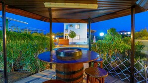 Eine Terrasse im Freien mit einem Holzfässchen als Tisch, umgeben von Grünpflanzen und einem Metallzaun.