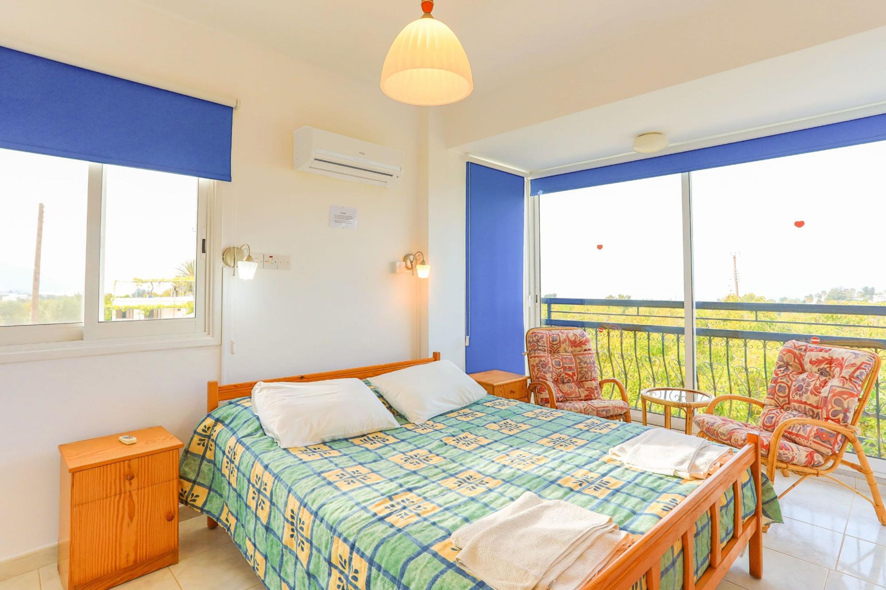 A bedroom with a bed, a nightstand, a chair, and a balcony with a view.