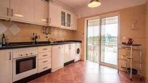 Een moderne keuken met witte kasten, een inbouwoven, een wasmachine en een grote schuifpui die uitkomt op een buitenruimte.