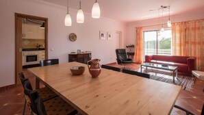 Een moderne woonkamer met een houten eettafel, een rode bank en een keuken op de achtergrond.