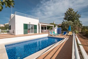 A swimming pool with a white building and green shutters in the background.
