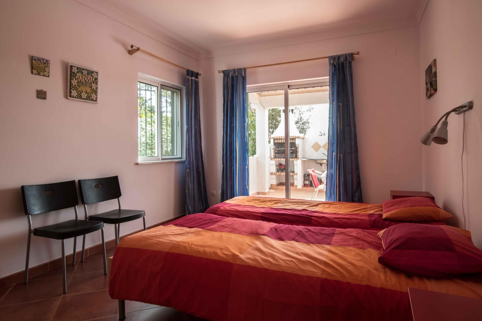 Ein Schlafzimmer mit einem Bett, zwei Stühlen, einem Fenster und Blick ins Freie.