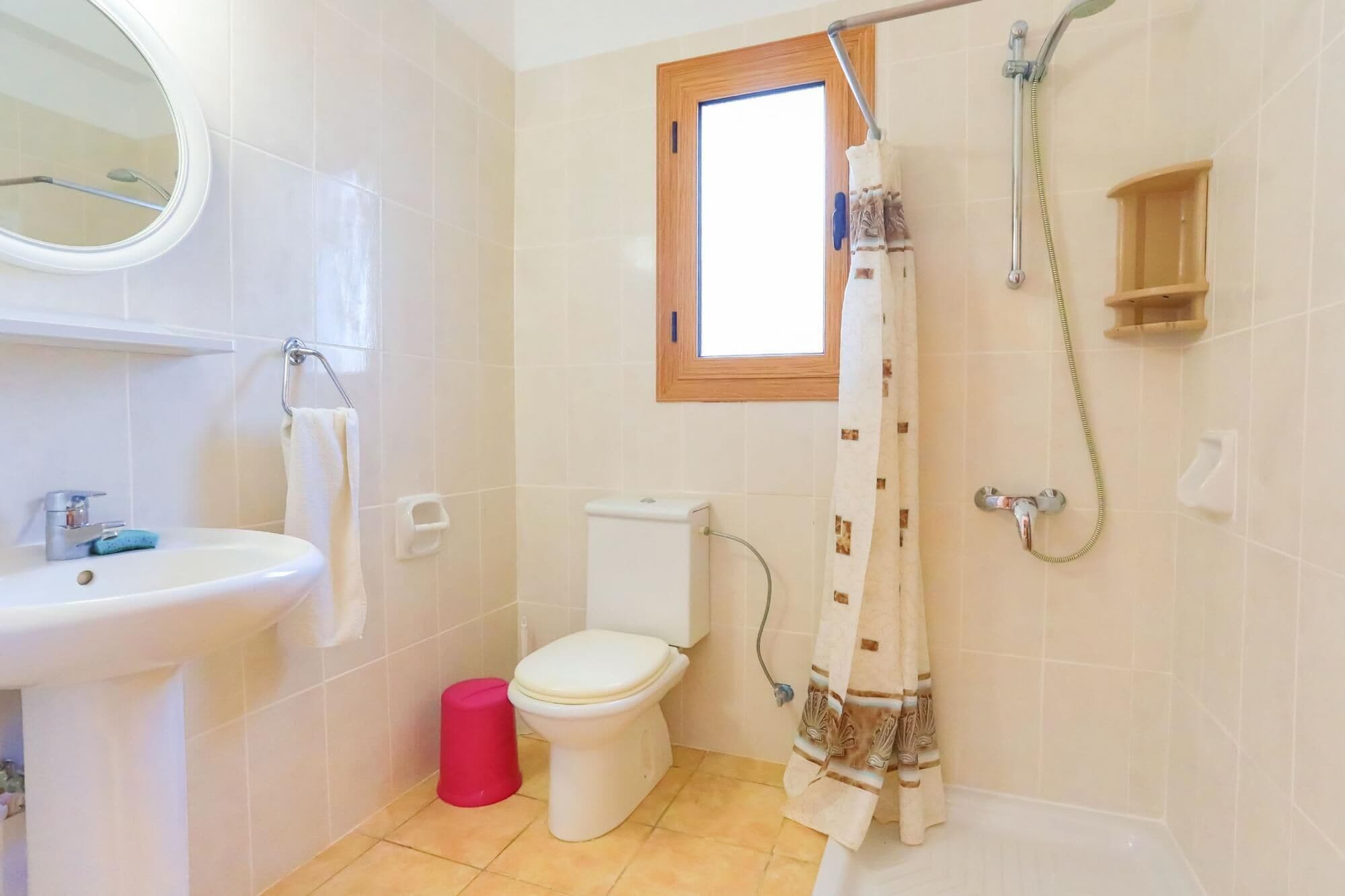 A bathroom with a sink, toilet, shower, and a window above the toilet.