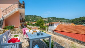 A patio with a table set for breakfast, a bench, and a staircase leading to a balcony. - Sterna Studio in Gaios (Paxos)